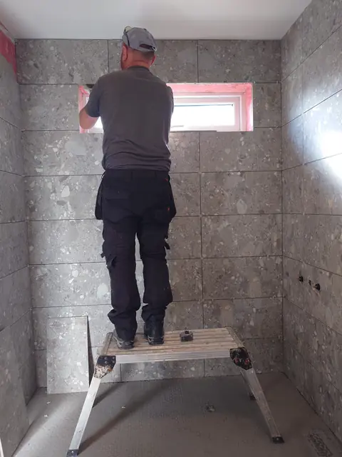 Damion on a platform finishing the top course of a full-height tiled wall
